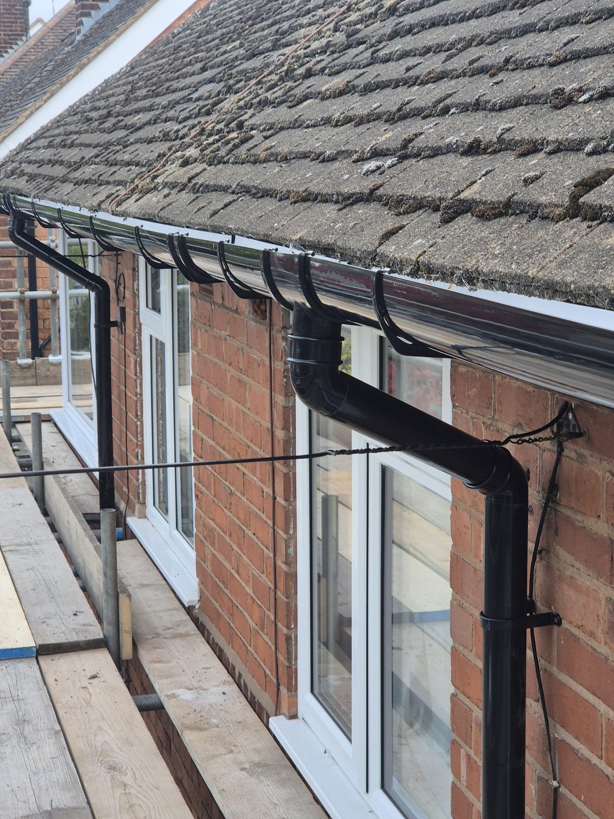Black gutter and downpipe fitted along a tiled roofline
