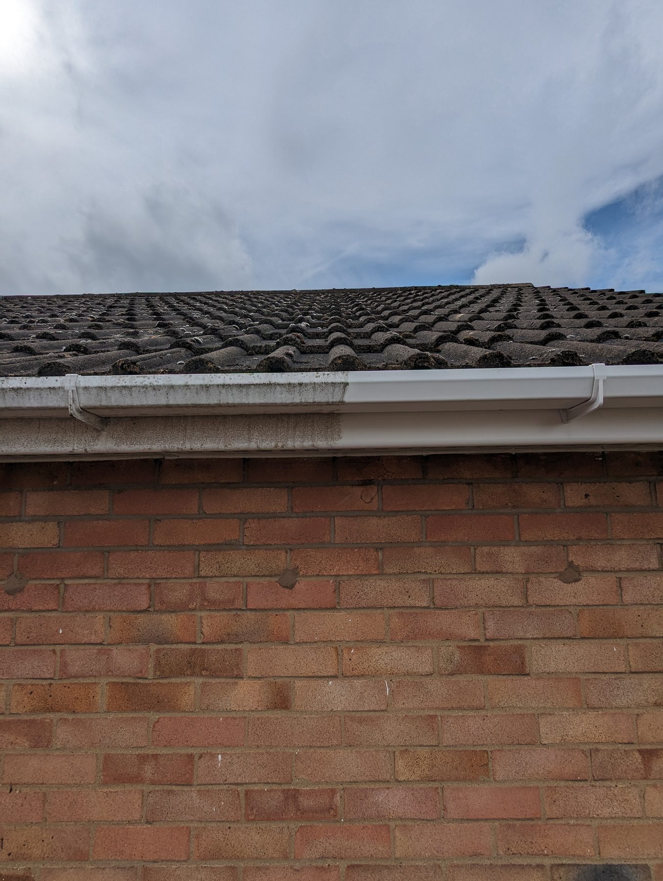 Sleek black UPVC gutter installed alongside aged tiles, overlooking a Warwickshire garden